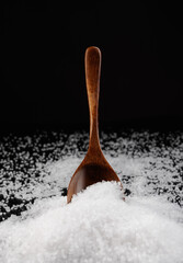 Wooden spoon inserted into a pile of salt. Table salt on a black background.