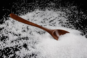 Wooden spoon inserted into a pile of salt. Table salt on a black background.