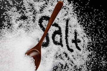 A wooden spoon inserted into a pile of salt. The inscription salt on the surface of the salt.