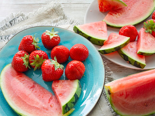 Juicy strawberries and watermelon slices on a turquoise plate and on a white wooden table. healthy refreshing snack. top view