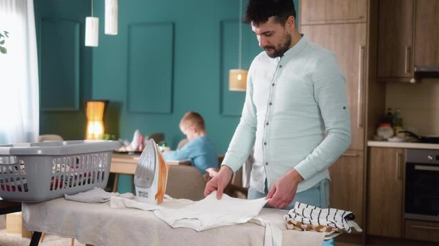 A young father is ironing laundry in the living room