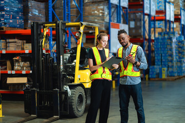 Two people are standing in a warehouse, one of them is reading a clipboard. The warehouse is filled with boxes and crates, and there is a forklift in the background. Scene is serious and focused