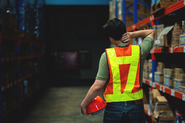 A man in a yellow vest and orange helmet is walking through a warehouse. He is wearing a reflective vest and a hard hat