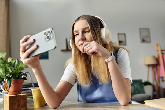 A teenage girl relaxes in her cozy room, engaging with her smartphone while wearing headphones.