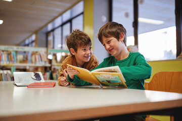 wo smiling boys reading a book together in a library.