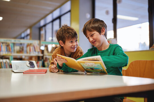 wo smiling boys reading a book together in a library.