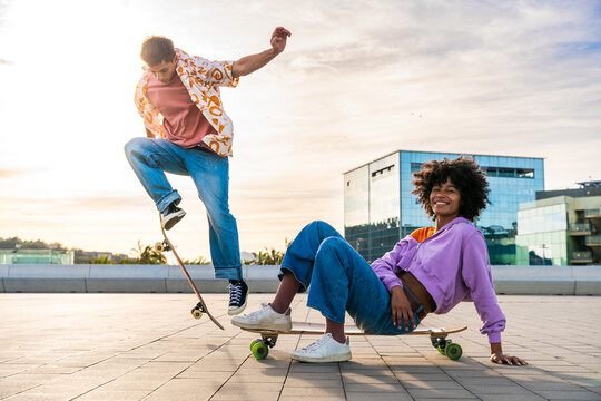 Young multiethnic modern couple with skateboards dating outdoors - Two friends having fun skating around city urban areas, concepts about youth, diversity, green trasportation and mobility