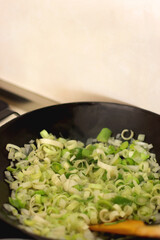 Sauteing chopped leek slices in a wok. Selective focus.
