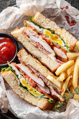 A delicious club sandwich featuring layers of grilled chicken, crispy bacon, fresh lettuce, tomatoes, and creamy mayonnaise, served with crispy French fries and a side of ketchup.
