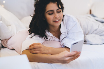 Beautiful woman checking network news after awaking using smartphone gadget and home internet...