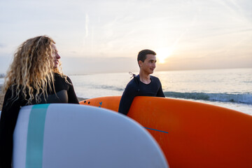 Fototapeta premium Two friends surfers going for surfing in the sea. Carrying surfboards running in to the sea surfing