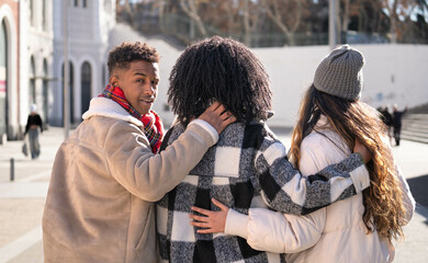 Fototapeta premium Three diverse students walking together in a friendly embrace, enjoying their time together on a sunny day in the city