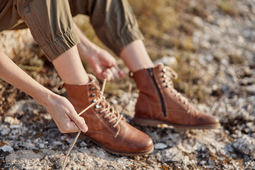 Woman tying boots on rocky hillside during adventure travel hike in the mountains
