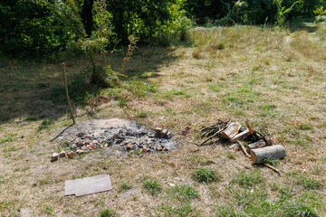 Abandoned campfire site with ashes, logs and scattered bricks in a grassy field surrounded by trees.