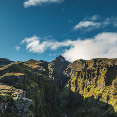 Majestic view of Mulagjufur Canyon in South Iceland, showcasing steep cliffs, flowing stream, and a hidden waterfall under a vibrant sky.