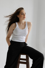 Young woman sitting on stool posing in studio with white background