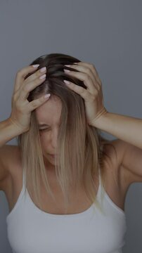 Young blonde woman feeling dizzy suffering from a severe headache holding her head with hands on dark grey background. Dizziness, vertigo, fatigue, low blood pressure, anemia, migraine. Vertical video