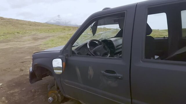 Crashed, broken car abandoned in desert. Shot inside car of steering wheel, panel, cracked windshield. Car damaged in accident without wheels and windows is rusting in midst of wilderness nature