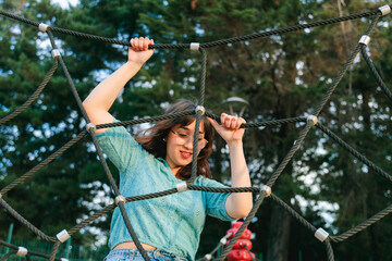 Young woman climbing rope net in playground at park