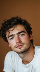Fototapeta premium A portrait of an attractive young man wearing a white t-shirt, looking at the camera with soft lighting and warm tones, he has dark brown hair styled in waves