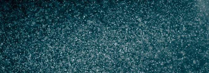 Defocused particles floating on a turquoise background, creating a sparkling and dreamy atmosphere
