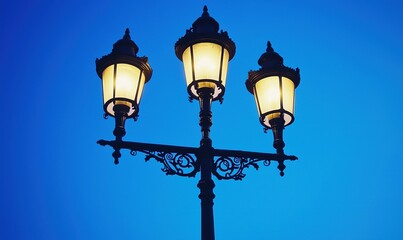 Three glowing street lamps against a twilight blue sky, ideal for urban or historical settings
