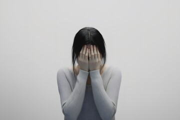 Scared woman hiding her face with hands, conveying deep fear and shame against a stark white background, reflecting emotional turmoil