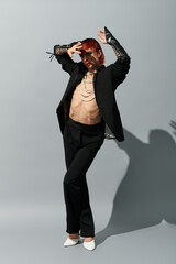 A young man with striking features and vibrant hair displays a daring outfit while posing.