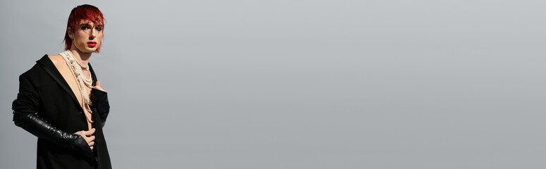 A young man with red hair stands confidently in a stylish outfit against a neutral background.