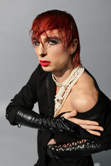 A young man exudes confidence with vibrant red hair and striking makeup, wearing a daring ensemble.