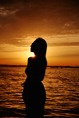Fototapeta premium silhouette of a young girl in sunglasses relaxing by the sea during sunset