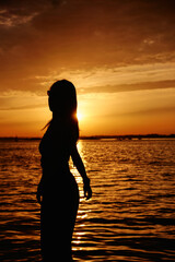 silhouette of a young girl in sunglasses relaxing by the sea during sunset