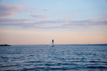A sailing yacht floats on the waves of a river during sunset on a summer evening