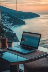Obraz premium Picture of a laptop on a table overlooking a beautiful sunset and the ocean.