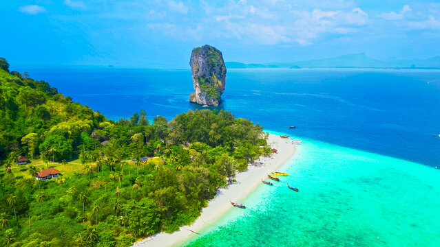 Top aerial drone view of a paradise beach, crystal clear turquoise ocean, cliff, white sand, and longtail boats in Thailand. Ko Poda island from above.