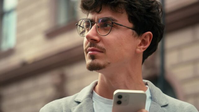 Serious male Hispanic man guy holding smartphone looking around searching location address waiting taxi online internet GPS navigation outside in city street outdoor looking in mobile phone outdoors