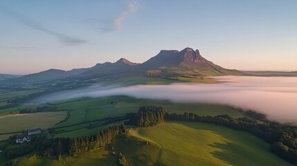 Aerial view of a misty mountain range bathed in sunrise light, with a vibrant blue sky completing the peaceful scene.