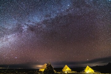 Galactic starry night meteor shower captured above desert tents during clear skies