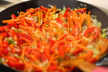 Stir frying chopped leek, carrots and red bell peppers in a wok. Selective focus.