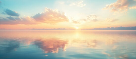 Obraz premium Glassy lake at sunrise with pastel pink and blue clouds reflecting on calm water and ample empty space for text in the background