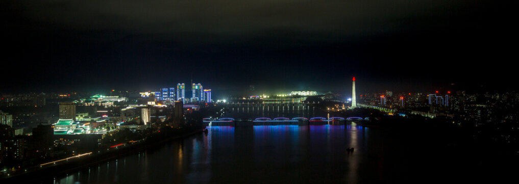 New modern buildings illuminated at night in front of the Juche tower, Pyongan Province, Pyongyang, North Korea