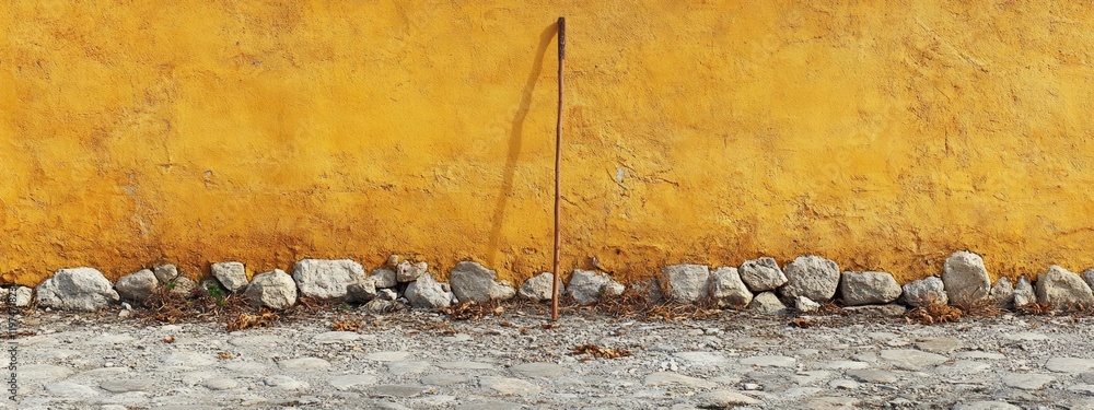 Poster textured yellow wall with rocks and a vertical stick in front, featuring ample copy space for text p