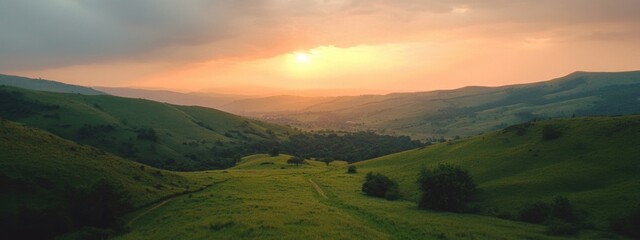 Fototapeta premium Sunset over rolling green hills with a valley and trees in the foreground showcasing natural landscape and serene atmosphere Copy Space