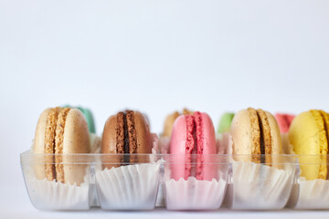 French Macarons with white paperpan in plastic transparent packaging box on gray background, colorful cakes with various flavors. appetizing dessert, macaroons. Copy space for text, side view