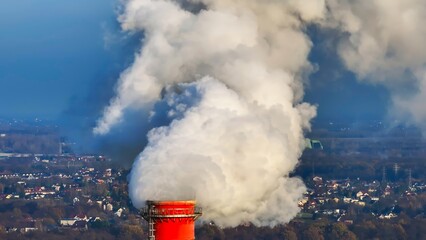 Industrial smoke rises from a chimney, contributing to air pollution amid a city landscape under a...