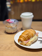 Plate of croissant and yogurt dessert on a wooden table. A hot beverage in a white cup adds warmth to the casual dining scene. Breakfast in coffee shop