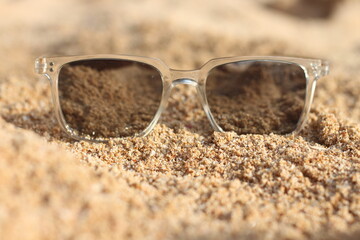 A white sunglass placed on the beach on holiday. Stylist black sunglasses on sand.