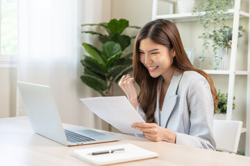 Happy cheerful asian young woman holding paperwork, reading tax refund paper bill, receive good...