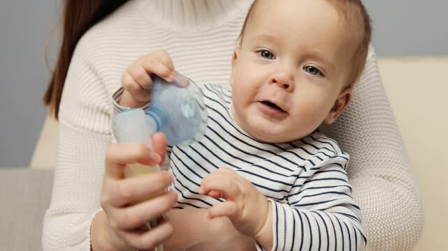 A young child is receiving respiratory treatment through a nebulizer while being held by a parent. The child appears curious and engaged during the process