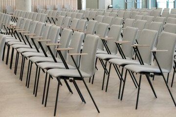 
An empty fragment of a conference hall or auditorium with rows of gray chairs with wooden arms.